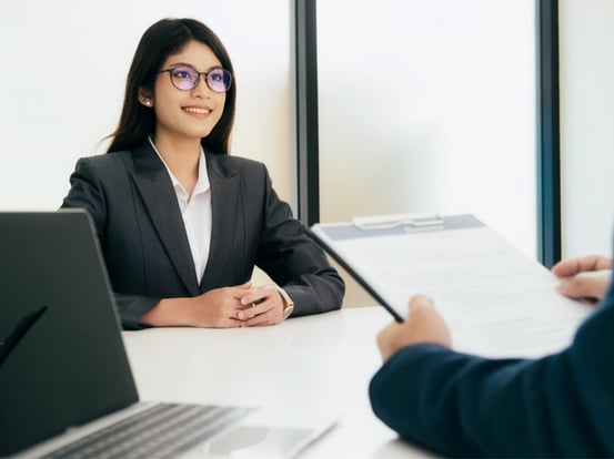 Woman in business suit smiling at person holding clipboard