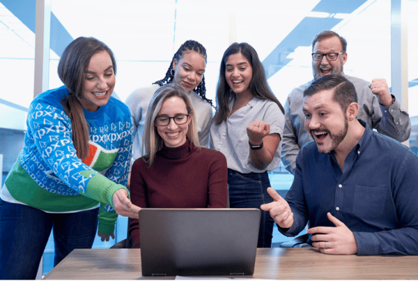 men and women sitting and standing while staring at laptop