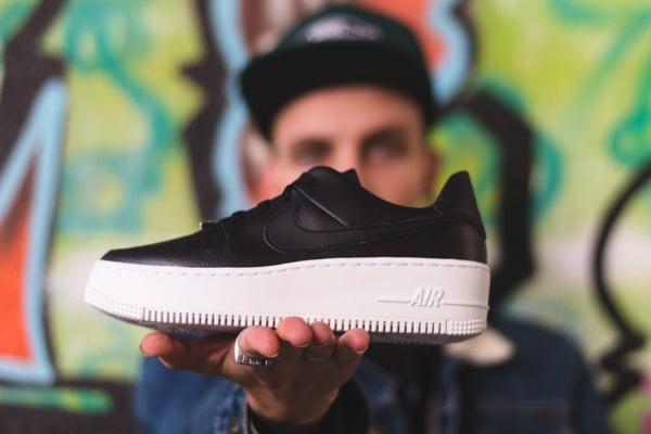 shallow focus photography of black unpaired white and black Air Forced 1 shoe on man's hand