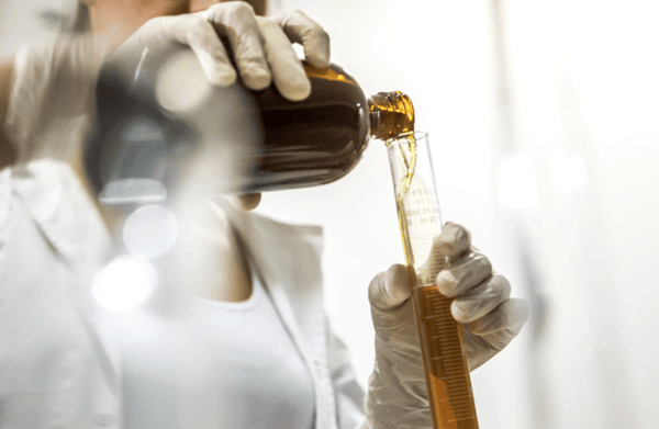 woman wearing white lab coat holding brown bottle and glass tube