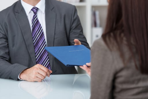 Employment interview with a close up view of a female applicant handing over a file containing her curriculum vitae to the businessman conducting the interview