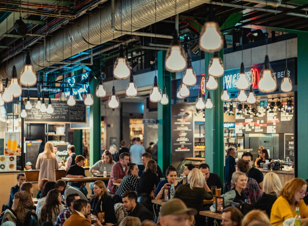 people sitting and others are standing inside coffee shop showing lighted ceiling lamps