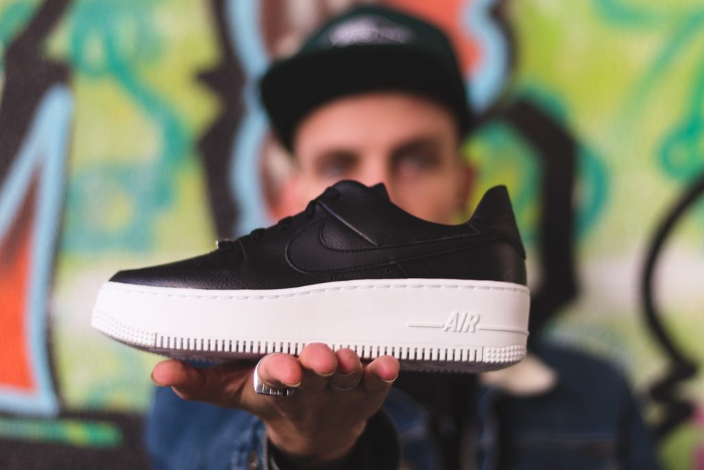 shallow focus photography of black unpaired white and black Air Forced 1 shoe on man's hand